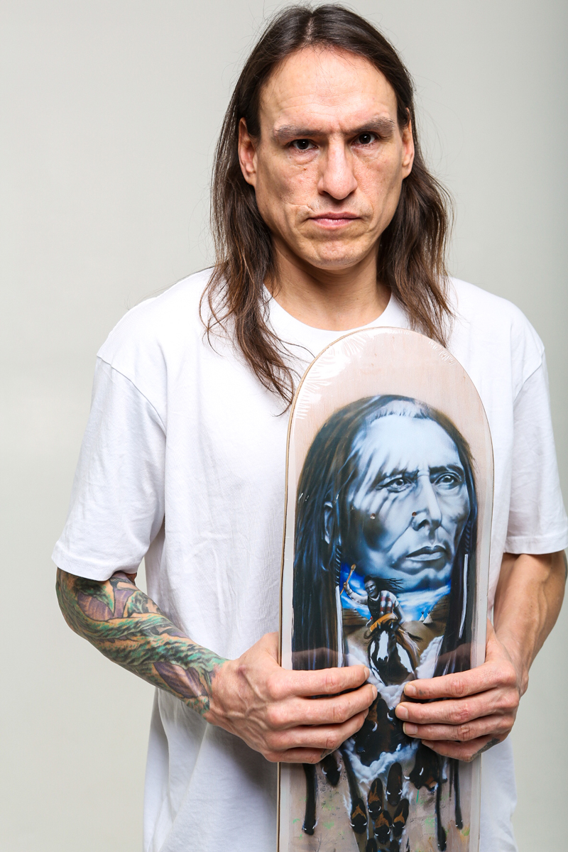 portrait photo of Joe Buffalo holding his Pitikwahanapiwiyin (Poundmaker) pro-model board.