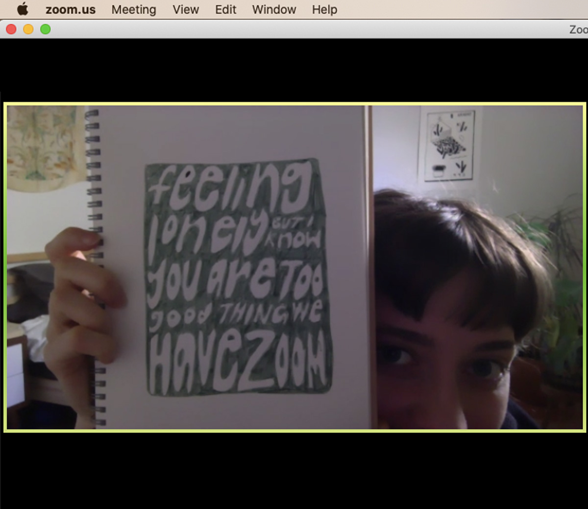 screenshot off of a Zoom video call where Julia is holding up her sketchbook with an illustration that says "feeling lonely but I know you are too good thing we have Zoom".