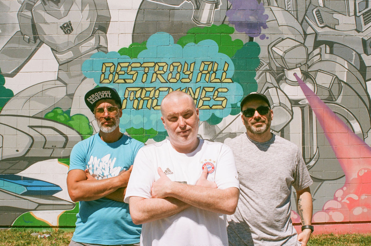 portrait photo of (from left to right) Dedos, Jay Swing, and FlipOut standing in front of a mural done by the AA Crew.